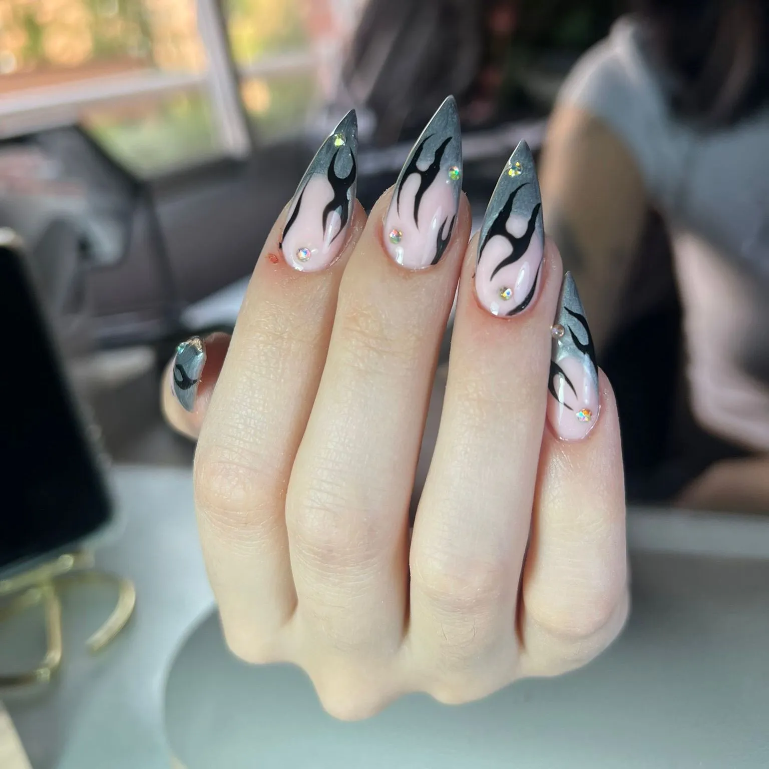 Uñas stiletto grises con diseño de llamas negras y cristales